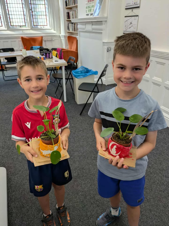 Two children each holding a small plant in a handmade pot.