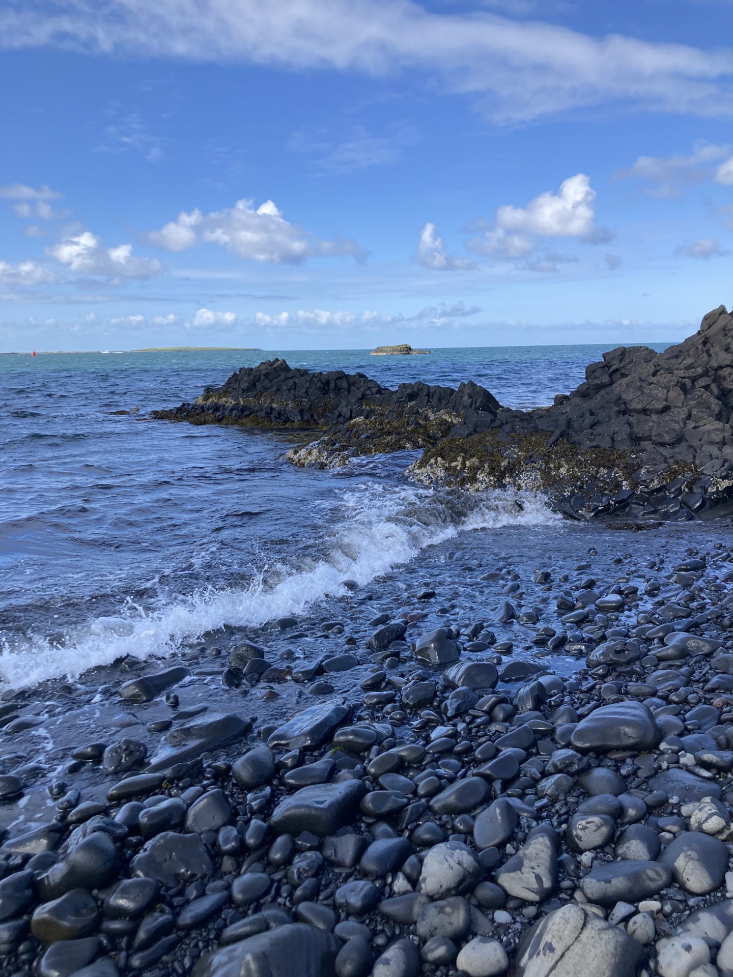A photograph of a pebbled beach with small waves.