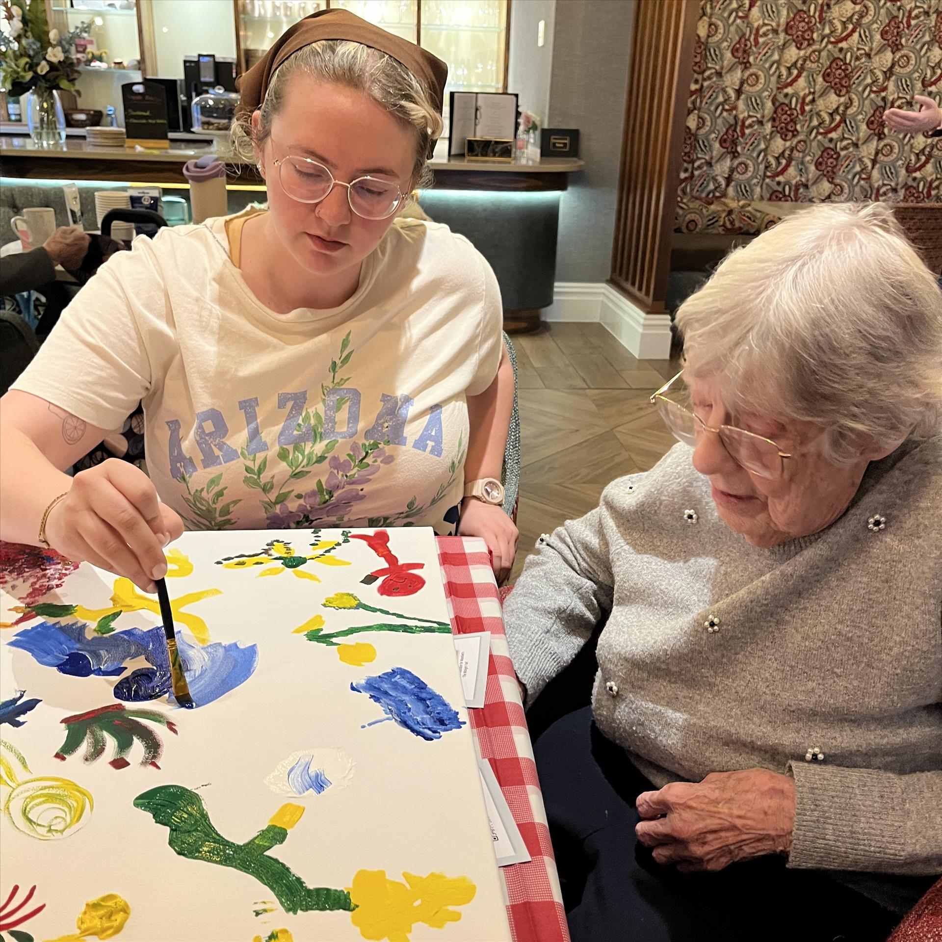 A young woman painting on a large canvas with an older woman. 