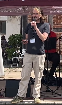 A young person stood in front of a gazebo, holding a microphone and reading poetry. 