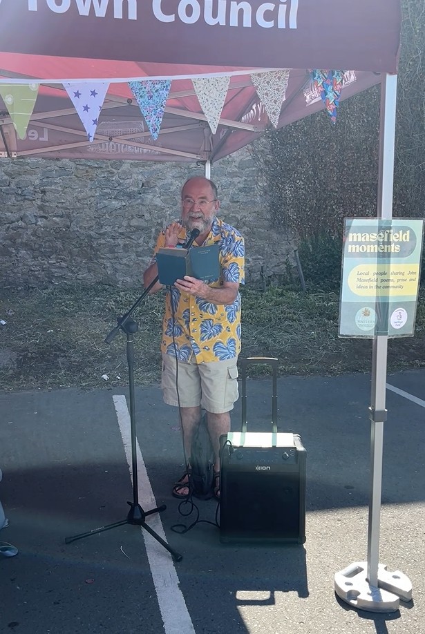 A man stood in front of a gazebo, holding a microphone and reading poetry. 